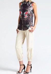 Blusa sin mangas en negro con estampado floral; pantalones cremados ajustados; tacones negros con tiras. Cuenta con cierre de botones y acentos decorativos.