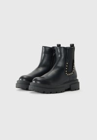 Schwarze Leder-Stiefeletten mit dicken Sohlen, Seiteneizipern, elastischen Einsätzen und goldenen Nietenverzierungen rund um die Einsätze auf einem weißen Hintergrund.