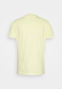 T-shirt en coton jaune clair uni à manches courtes, vu de dos sur un fond blanc uni.