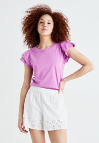 Rosa bomulls-T-skjorte med korte puff-ermer, kombinert med hvite shorts med bølgekant og detaljer med øyelet broderi.
