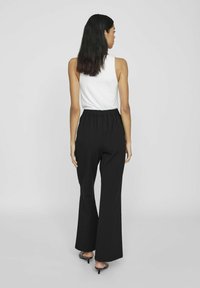 Črne flare hlače z elastičnim pasom, lahka tkanina in gladka tekstura. Nosi se z belim brezrokavnikom.