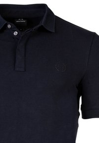 Námořnická modrá polo košile vyrobená z texturované tkaniny, se dvěma knoflíky na légu, krátkým rukávem a malým raženým logem na hrudi.