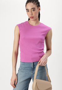Rosa ribbet stram top uten ermer med rund halslinning. Modellen holder en beige skulderveske, kombinert med lyseblå dongeribukser.