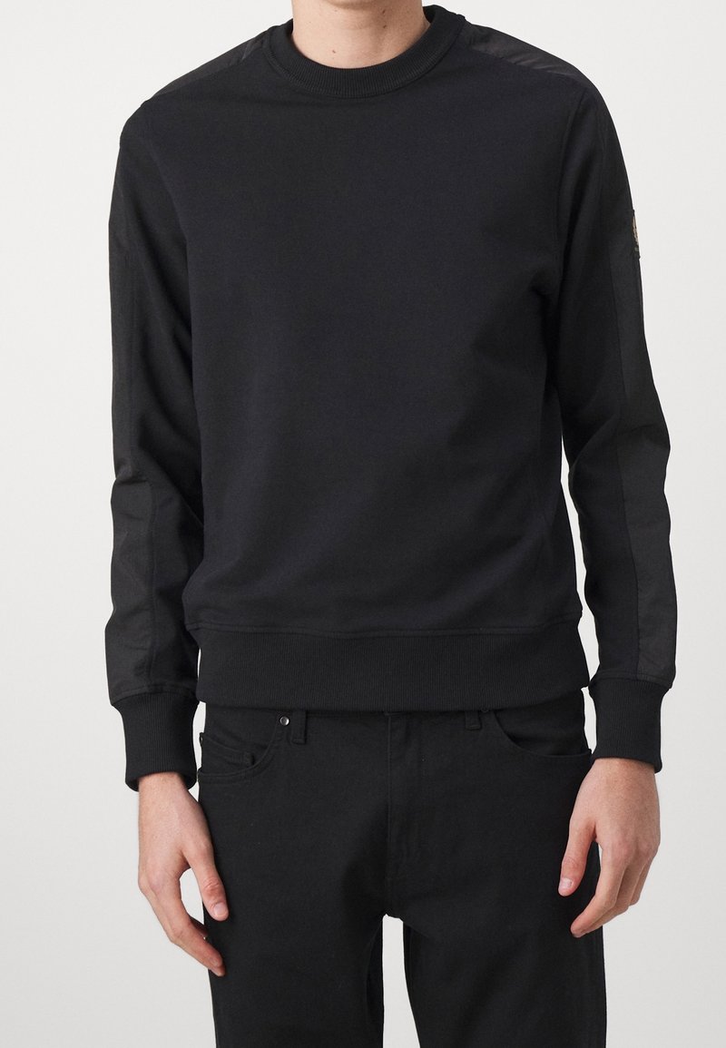 Svart sweatshirt med rund halsringning, med långa ärmar som har kontrasterande materialpaneler samt ribbade muddars och nederkant. Slät textur.