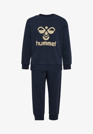 Marineblauwe katoenen trainingsoutfit met lange mouwen en broek. Heeft een beige logo ontwerp op de voorkant. De boorden en tailleband zijn geribbeld.