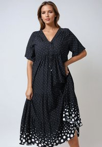 Zwarte jurk met witte stippen, V-hals, korte mouwen, gathered taille en een gelaagde rok met grotere stippen aan de zoom. Lichtgewicht stof.