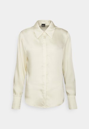 Blusa de satén color crema de manga larga con cuello puntiagudo, tapeta de botones oculta y puños abotonados sobre un fondo liso.