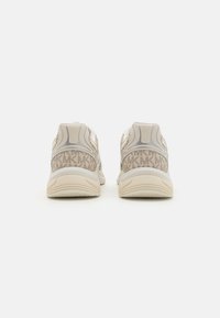 Lyse beige treningssko med en teksturert mesh-overdel, kontrasterende grå detaljer og mønstrete utsmykninger på hælen, med en polstret såle.