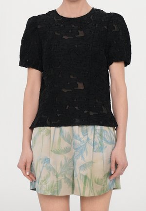 Sort blonde top med puffede ærmer har et blomsterpræget design. Kombineret med lyse shorts med palmeblad mønstre.