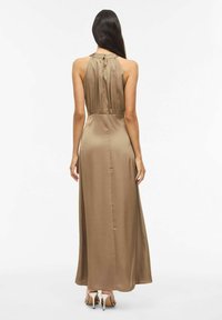 Robe longue sans manches en satin couleur beige avec un col licou, taille froncée et jupe longue jusqu'au sol. Texture lisse et détails de style simples.