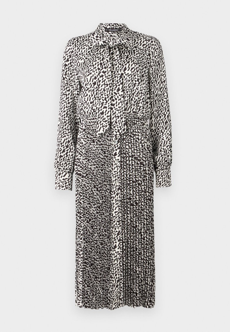 Schwarz-weiße gemusterte Kleid mit Kragen, langen Ärmeln, Bindeband am Hals und gefälteltem Rock, aus leichtem Stoff gefertigt.