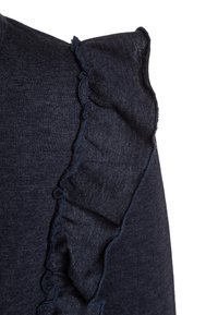 Námořnická modrá blůza s volánkovým detailem na ramenou, vyrobená z měkké látky. Má texturovaný povrch a čistý, jednoduchý design.