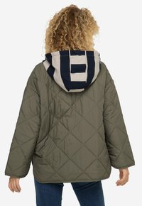 Giacca trapuntata verde oliva con cappuccio a righe in navy e crema, caratterizzata da una silhouette rilassata e spalle scese.