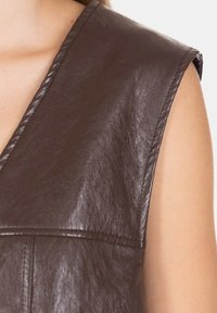 Top in finta pelle marrone con scollatura a V, linea delle spalle pronunciata e dettagli di cucitura visibili sulle cuciture e sui pannelli.