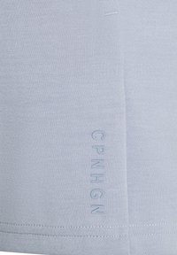 T-shirt aderente azzurro chiaro realizzato in tessuto liscio, con testo in rilievo "CPNHGN" sul lato. Design semplice con linee pulite e senza motivi.
