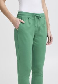 Groene joggingbroek met een verstelbare tailleband, zijzakken en een zachte, gestructureerde afwerking. Tapered pijpen en plooi-details aan de voorkant.