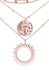 Collier en rose gold à plusieurs couches, présentant un pendentif rond avec une surface texturée et un motif de soleil entouré de rayons allongés autour d'un centre vide.