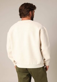 Crèmekleurige, gestructureerde trui met een ronde hals en ribgebreide manchetten, van achteraf gezien, in combinatie met olijfgroene broek.