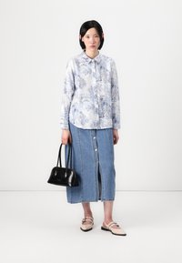 Cămașă cu imprimeu floral albastru deschis, fustă din denim cu nasturi în față, geantă neagră și pantofi bej cu bretele. Design simplu și modern.