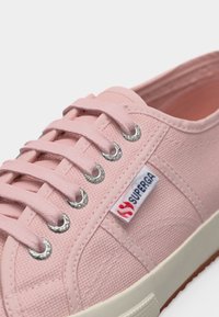 Nahaufnahme eines rosa Superga-Leinenschuhs mit Schnürsenkeln, Metallösen, Gummisohle und Markenlabel an der Seite.