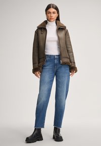 Bruine leren jas met een zachte bontkraag en manchetten, gecombineerd met medium-was denim jeans en zwarte grove laarzen.