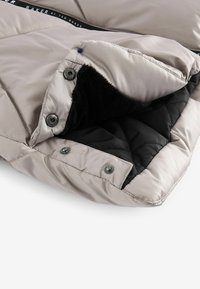 Giacca puffer trapuntata con un morbido interno nero, esterno grigio chiaro e bottoni a scatto. Presenta una texture liscia e fodere a contrasto.