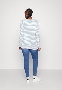Long-sleeve striped top in white and light blue, featuring a rounded neckline. Paired with fitted blue jeans and white sneakers.