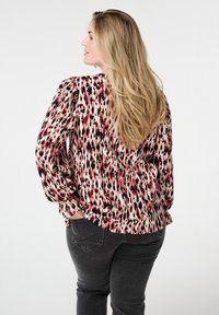 Blouse à manches longues avec un motif abstrait rouge, noir et rose, fabriquée en tissu léger, présentant des détails froncés sur les manches.