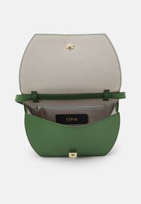 Zelená kožená kabelka s klopou, s béžovým interiérem, zlatými doplňky a malou zipovou kapsou. Značková etiketa je viditelná uvnitř.