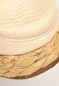 Gros plan d'une semelle en cuir beige fixée à une plateforme tressée en paille avec des coutures visibles et des détails de texture.
