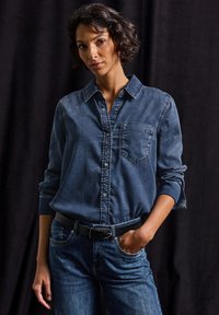Diverse Jeanshemd in Dunkelblau, mit einer Brusttasche und langen Ärmeln. Kombiniert mit blauen Jeans und einem schwarzen Gürtel. Strukturierter Stoff.