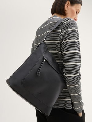 Donna che indossa un maglione a righe bianco e nero con una grande borsa a tracolla in pelle nera con tasca anteriore con cerniera.