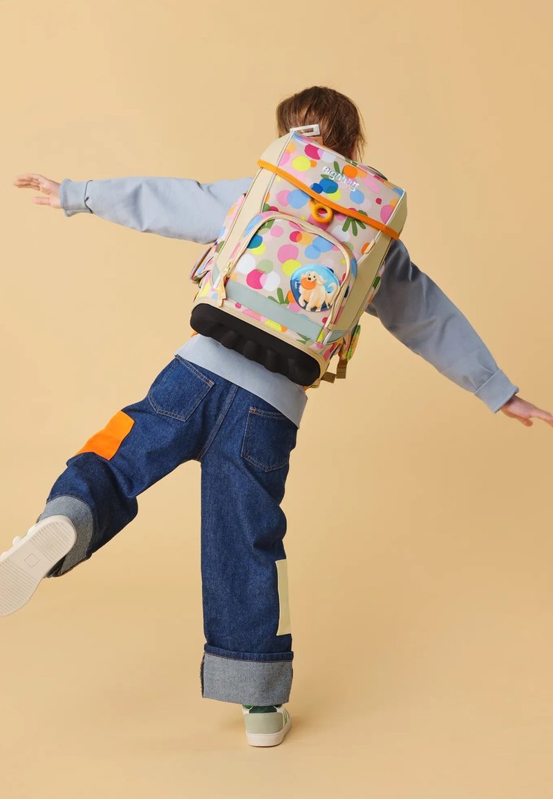 Sac à dos coloré à pois, avec un patch de chien en cartoon. Fabriqué en tissu, il possède des bretelles réglables et un compartiment principal avec un rabat.