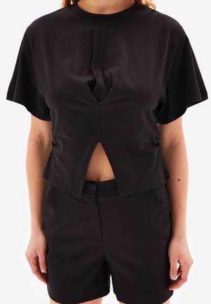 Femme portant un haut noir à manches courtes avec une découpe en forme de V à l'avant et un short noir taille haute assorti.