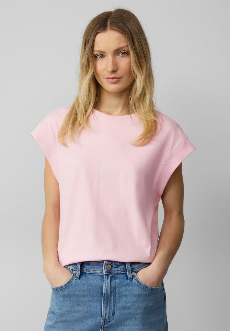 Lichtroze katoenen T-shirt met kapmouwtjes en een ronde halslijn, met een relaxte fit en een gladde textuur. Ggedragen met blauwe denim korte broek.