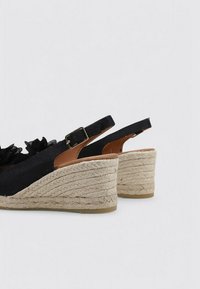 Sandalias de cuña negras con parte superior de tejido texturizado, tacón de yute trenzado y correa adjustable con hebilla de metal.