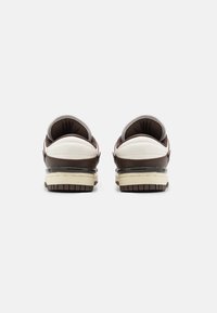 Bruna och vita sneakers med en slät läderöverdel, vadderad ankel och strukturerad sula. Har en krämfärgad mellansula och kontrasterande detaljer.