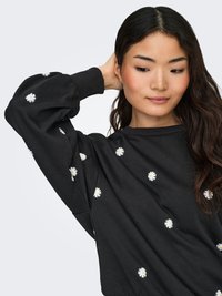 Black sweatshirt with white daisy embroidery, featuring a crew neck and long sleeves. Soft fabric with a relaxed fit and ribbed cuffs.