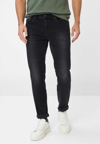 Schwarze Jeans aus Denim mit Slim Fit, ausgestattet mit normalen Taschen, einem Knopfverschluss und umgeschlagenen Bündchen, kombiniert mit weißen Sneakers.