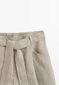 Pantaloni in lino beige con cintura in tessuto annodata e tasca laterale visibile, che mostrano un design casual e testurizzato.