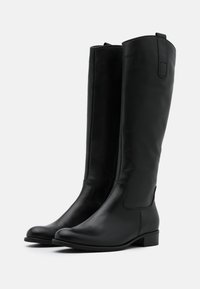 Bottes noires en cuir, montant jusqu'au genou, avec un bout rond, des coutures minimales, un petit talon et des tirants pour un enfilage facile. Texture lisse et design épuré.