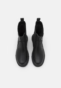 Botines negros de tobillo hechos de cuero suave, con paneles laterales elásticos, lengüetas y suelas de goma texturizada para agarre y durabilidad.