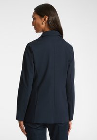 Granatowa marynarka dopasowana z klapami, gładką teksturą i długimi rękawami. Posiada dopasowane plecy i subtelne detale szwów.
