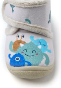 Zapatilla suave de tela color beige con forro de peluche beige, que presenta diseños de monstruos de dibujos animados coloridos en azul, verde, marrón y verde azulado.