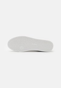 White sneaker with a textured rubber sole featuring a zigzag pattern, flat profile, and minimalistic design, suitable for casual wear.