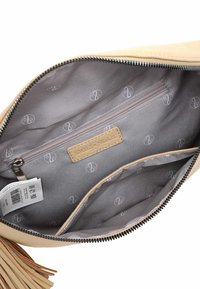 Beige leren tasinterieur met grijze voering, een ritsvak en een logo patroon. Accented met franjes en een metalen rits.