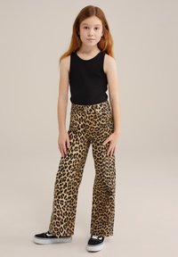 Juodas be rankovių marškinėlis, leopardų rašto plačios kelnės ir juodi sportbačiai. Lygus audinys su ryškiu gyvūnų raštu ir laisvas pritaikymas.