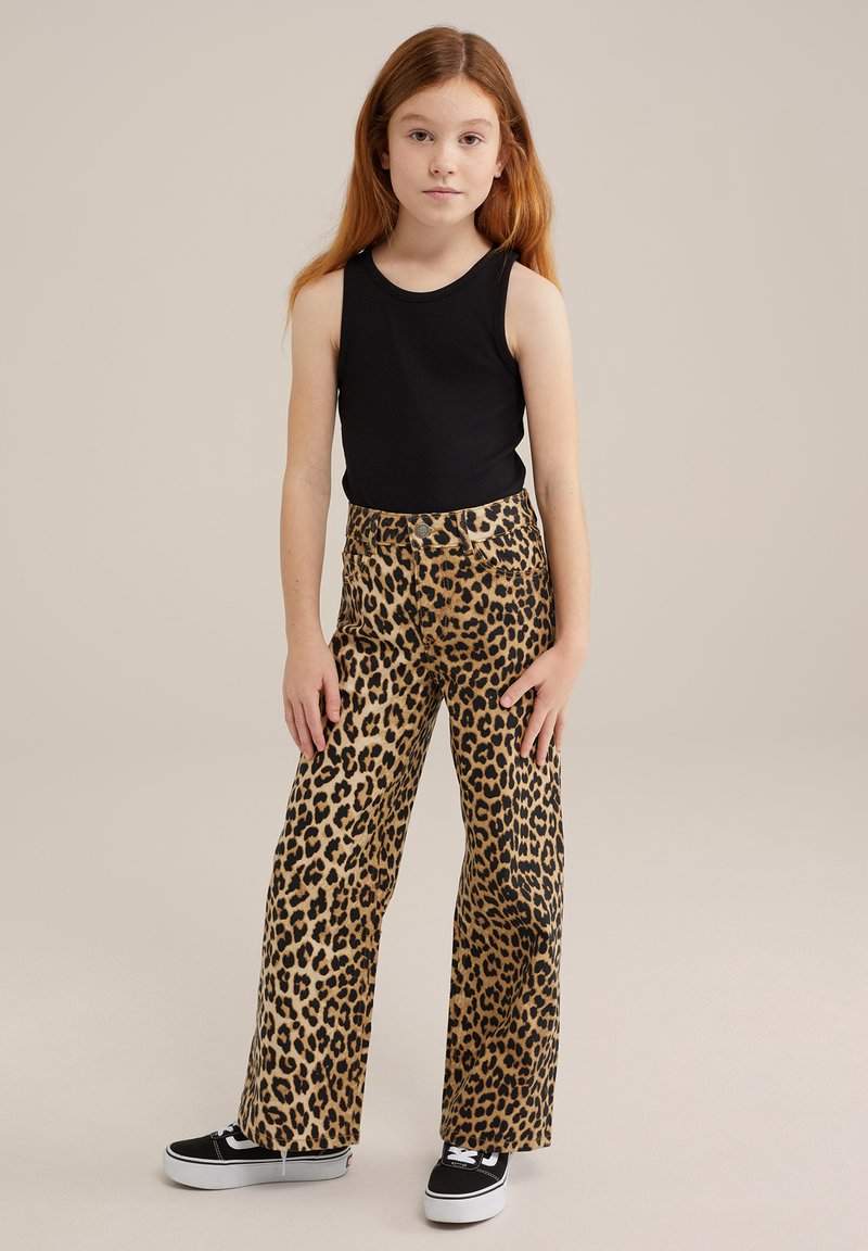 Juodas be rankovių marškinėlis, leopardų rašto plačios kelnės ir juodi sportbačiai. Lygus audinys su ryškiu gyvūnų raštu ir laisvas pritaikymas.