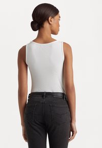 Bílý žebrovaný top bez rukávů s kulatým výstřihem, v kombinaci s tmavě šedými džíny s vysokým pasem, které mají černý opasek a detaily kapes.