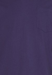 T-shirt viola a maniche corte realizzata in morbido cotone, con una piccola tasca sul petto a sinistra e una trama liscia e uniforme.